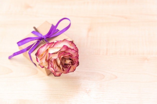 Caja de regalo con cinta lila y lazo sobre madera.