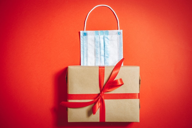 Caja de regalo con cinta y máscara protectora médica sobre fondo rojo. Copie el espacio.