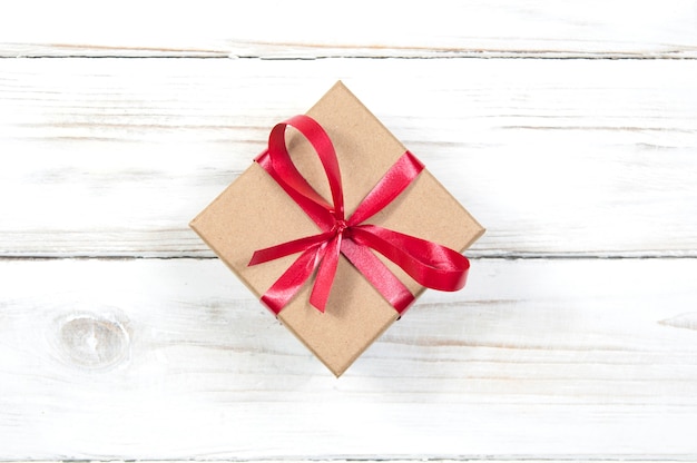 Caja de regalo con cinta roja y lazo en el centro de la imagen de cerca en una madera blanca