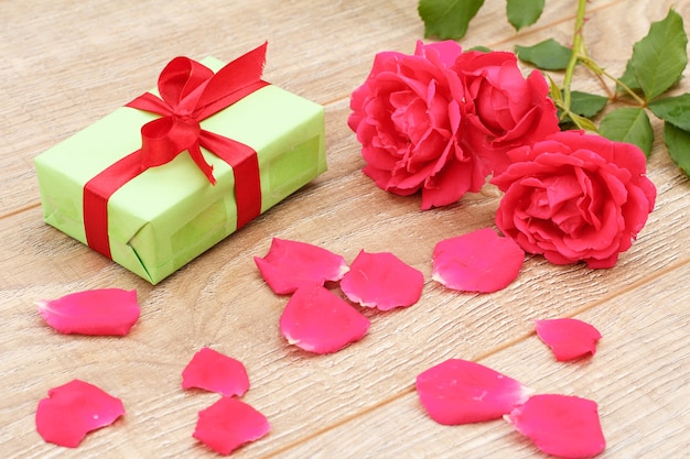 Caja de regalo con cinta roja, pétalos de rosa y hermosas rosas en el fondo de madera. Concepto de regalar en vacaciones. Vista superior.