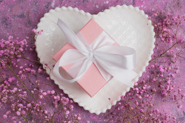 Una caja de regalo con una cinta rosa sobre un plato blanco en forma de platillo y un gypsophile.