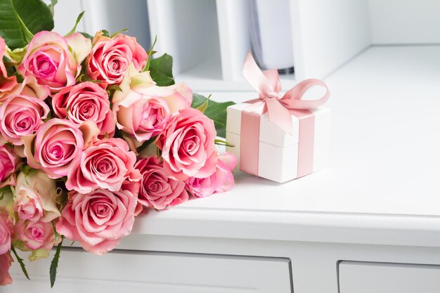 Caja de regalo con cinta rosada con flores de rosa en una mesa blanca