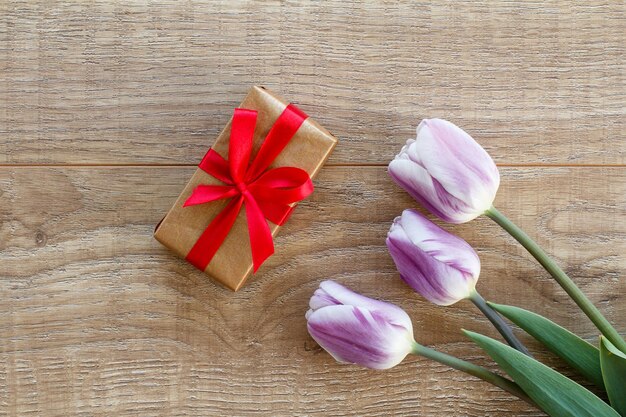 Caja de regalo con cintas rojas y hermosos tulipanes lilas Concepto de dar un regalo en vacaciones