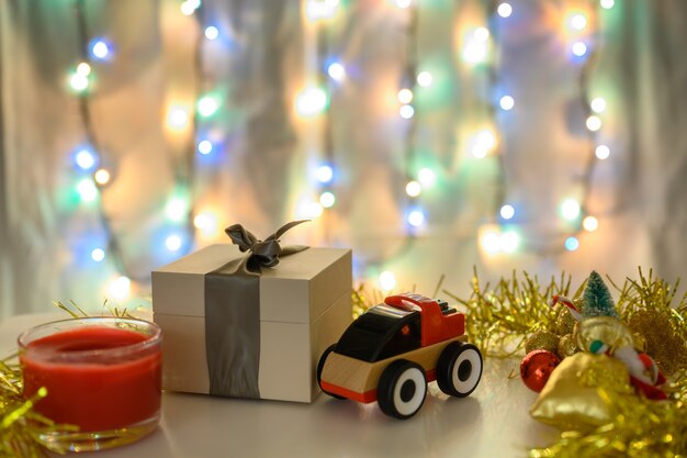 Caja de regalo y coche de juguete sobre un fondo de Navidad con una guirnalda brillante en colores fríos.