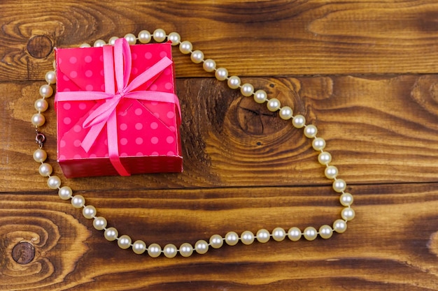 Caja de regalo y collar de perlas sobre fondo de madera