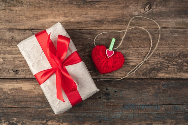 Caja de regalo y corazón rojo sobre fondo de madera.