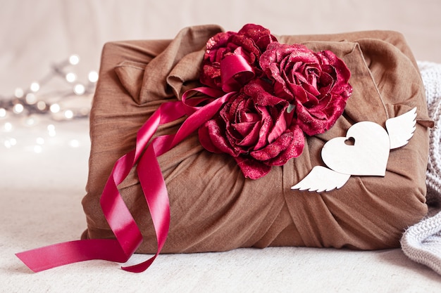 Caja de regalo decorada con cintas y rosas decorativas sobre artículos de punto. Envoltorio de regalo original para San Valentín.