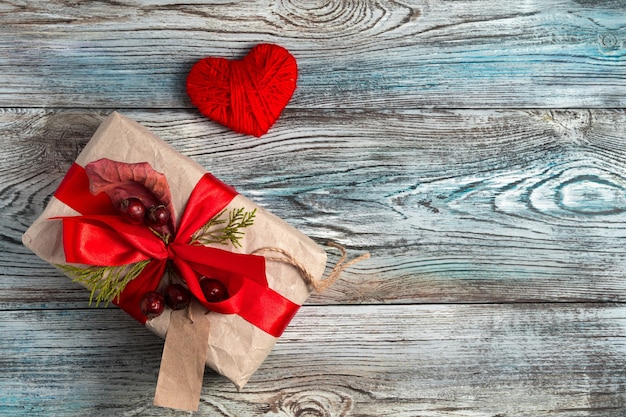 Caja de regalo decorada y corazón rojo sobre fondo de madera.