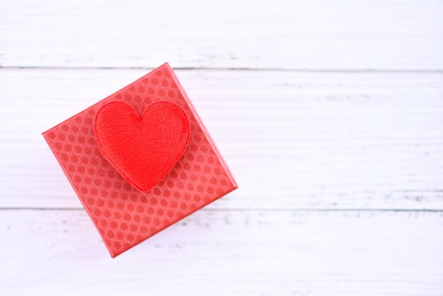 Caja de regalo decorada con corazón rojo sobre mesa de madera blanca