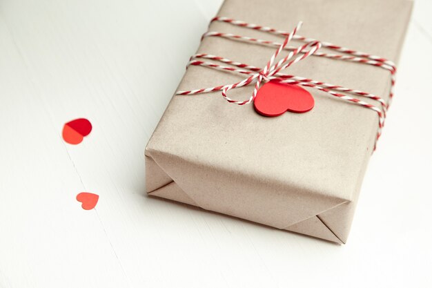 Caja de regalo del día de San Valentín decorada con corazones rojos sobre mesa de madera blanca