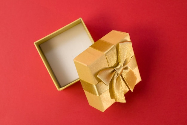 Caja de regalo dorada abierta con lazo de cinta dorada de seda sobre fondo rosa brillante