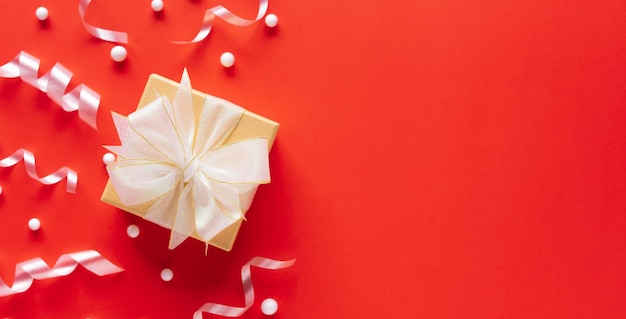 Caja de regalo dorada con cinta blanca con cinta rodante y nevadas sobre fondo de color naranja