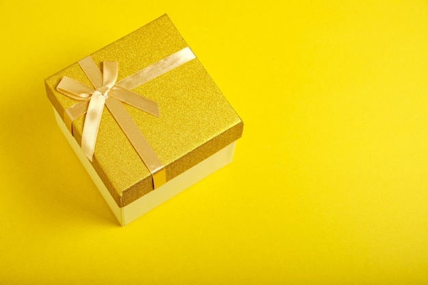 La caja de regalo dorada está atada con una cinta con un fondo amarillo de lazo