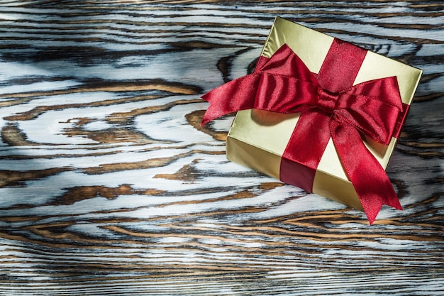 Caja de regalo dorada con lazo rojo en tablero de madera