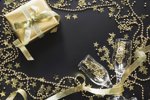 Caja de regalo dorado de lujo con dos copas de champán sobre fondo negro brillo. Fiesta de Navidad. Endecha plana. Vista desde arriba. Navidad.