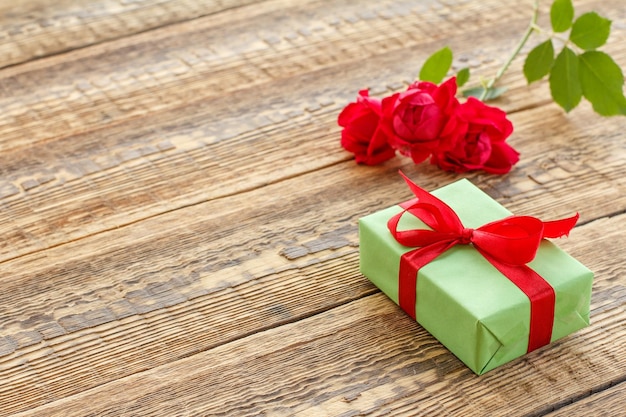 Caja de regalo envuelta con cinta en viejas tablas de madera decoradas con rosas rojas Vista superior con espacio para copiar