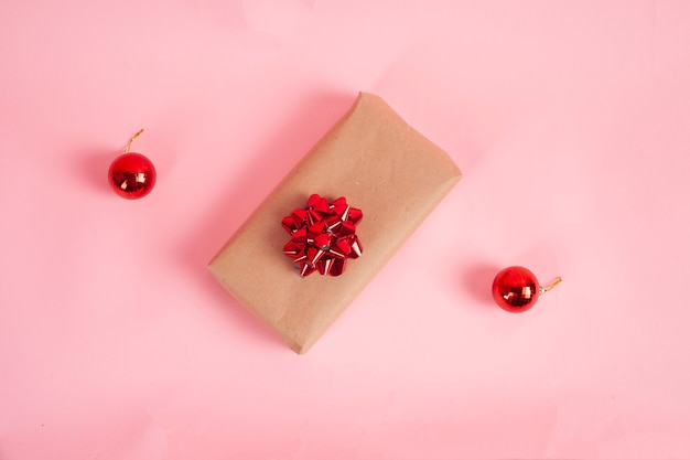 Caja de regalo envuelta en papel kraft y lazo rojo sobre fondo rosa Concepto de Navidad