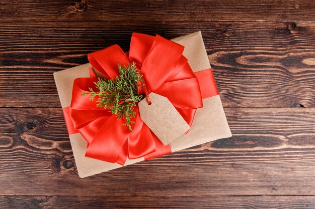 Caja de regalo envuelta en papel kraft reciclado con lazo de cinta roja y bola navideña sobre madera.