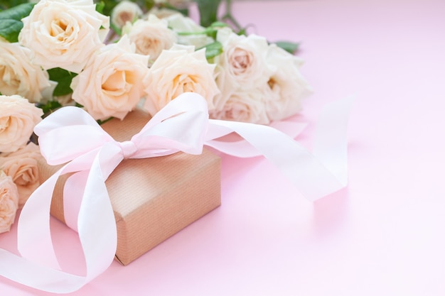 Caja de regalo envuelta en papel marrón con rosas rosadas sobre fondo rosa. Tarjeta de felicitación.