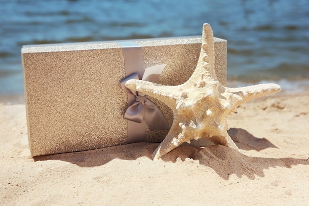 Caja de regalo con estrella de mar en la playa. Concepto de vacaciones de verano