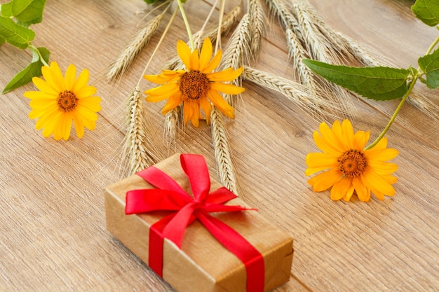 Caja de regalo, flores amarillas y espiguillas de trigo sobre tablas de madera. Vista superior.