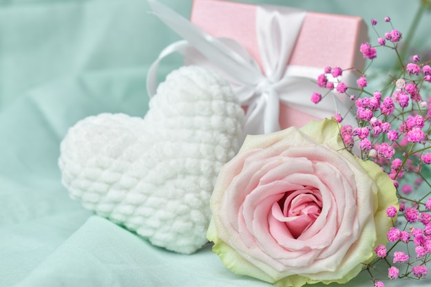 Caja de regalo con flores y corazón tejido de felpa blanca sobre fondo rosa.
