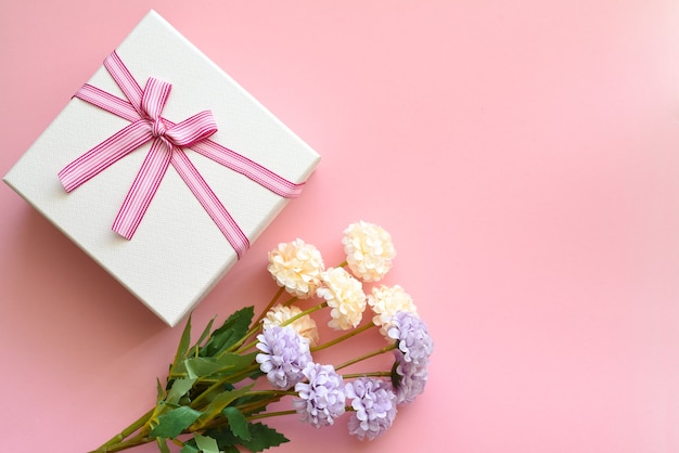 Caja de regalo con flores en una pared rosa.