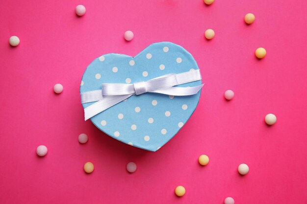 Caja de regalo en forma de corazón con caramelos sobre fondo rosa