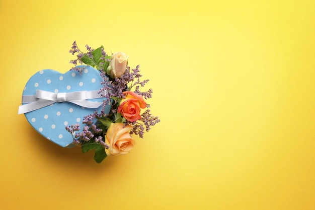 Caja de regalo en forma de corazón con flores sobre fondo amarillo