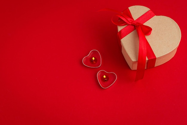 Caja de regalo en forma de corazón con lazo y dos velas sobre fondo rojo día de san valentín