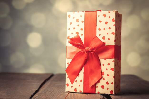 Caja de regalo con forma de corazón en la mesa de madera con bokeh de fondo.