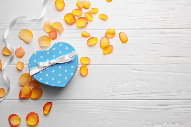 Caja de regalo en forma de corazón con pétalos de flores en la mesa de madera