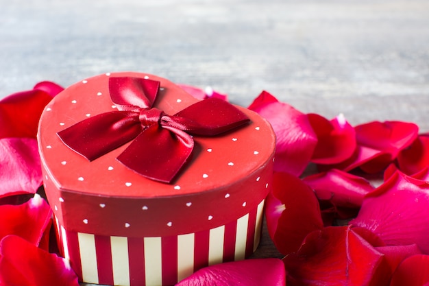 Caja de regalo en forma de corazón con pétalos en la mesa de madera