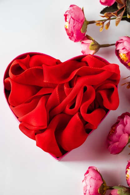 Caja de regalo en forma de corazón rojo y flores sobre fondo blanco.