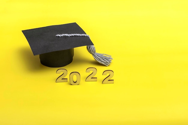 Caja de regalo en forma de gorro de graduación. Concepto de lanzamiento 2022 sobre fondo amarillo con espacio de copia