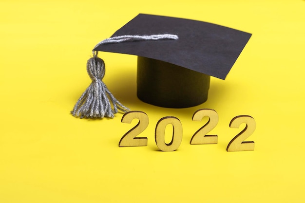 Foto caja de regalo en forma de gorro de graduación. concepto de lanzamiento 2022 sobre fondo amarillo con espacio de copia