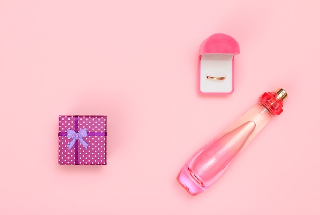 Caja de regalo, frasco de perfume y anillo dorado en caja sobre un fondo rosa. Cosmética y complementos para mujer. Vista superior.