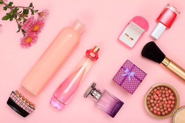 Foto caja de regalo, frascos de perfume y champú, horquilla, anillo dorado en caja, esmalte de uñas, polvo con pincel sobre fondo rosa. cosmética y complementos para mujer. vista superior.