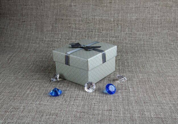 Caja de regalo gris con cristales artificiales azules y transparentes sobre un fondo gris