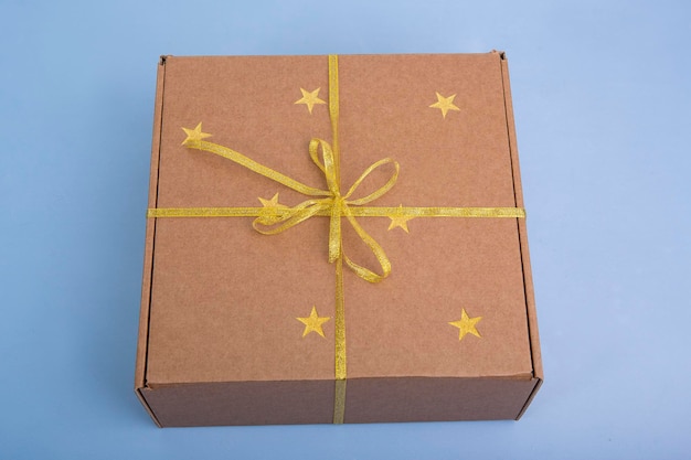 Caja de regalo kraft con cintas doradas y estrellas sobre fondo azul.