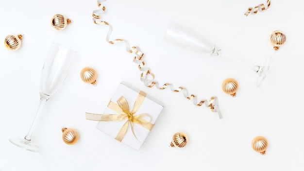 Caja de regalo de laicos plana dorada festiva copa de champán y bolas de navidad decorativas fondo blanco