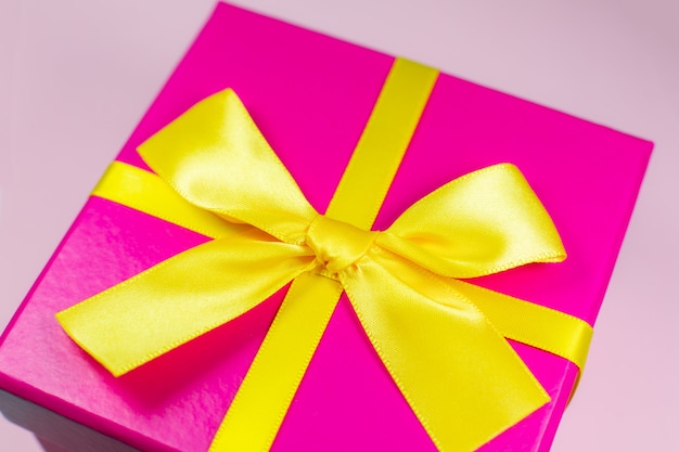 Caja de regalo con lazo amarillo sobre superficie rosa. Venta y descuento.