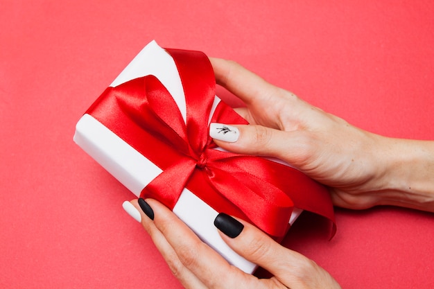 Caja de regalo con un lazo en las manos de una mujer sobre una superficie roja