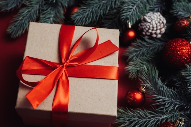 Caja de regalo con lazo rojo y ramita de árbol de Navidad sobre fondo rojo.