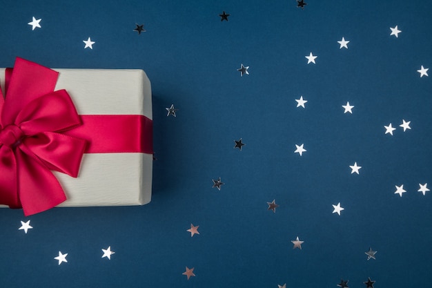 Caja de regalo con lazo rojo sobre fondo azul oscuro con estrellas plateadas. Concepto de vacaciones