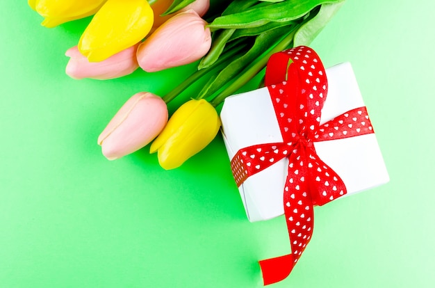 Caja de regalo con lazo rojo y tulipanes.