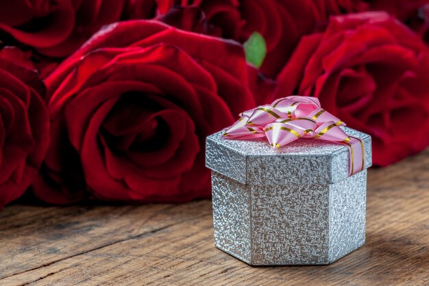 Caja de regalo con lazo rosa y rosas rojas detrás