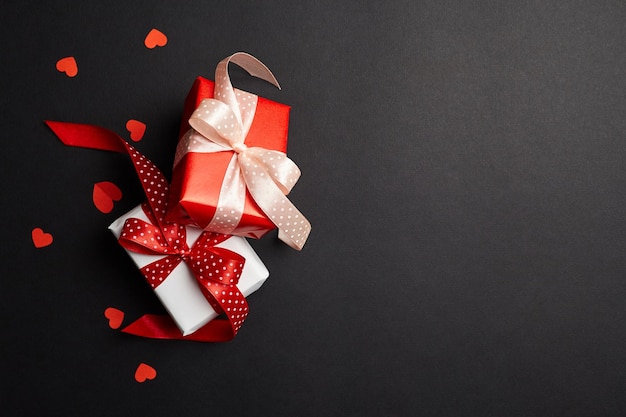 Caja de regalo con lazos y corazones de papel rojo sobre fondo negro con vista superior del espacio de copia Día de San Valentín