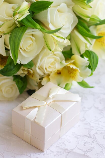 Una caja de regalo ligera con un lazo en el fondo de un ramo de rosas blancas