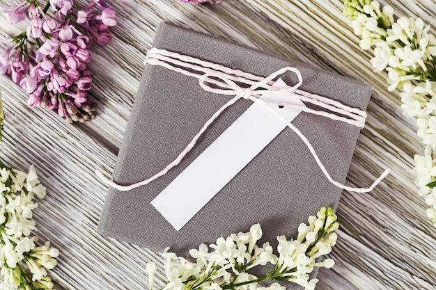Foto caja de regalo con lugar para firma o deseos decorada con una ramita y lila sobre madera vieja. estilo plano laico.